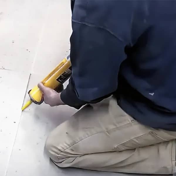 A man repairing using a yellow squeeze tube for concrete sealing.